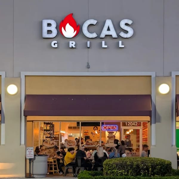 Exterior of Bocas Grill at night, with patrons dining outside and inside the brightly lit restaurant.