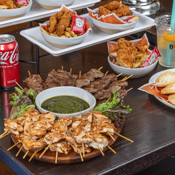 Bocas Grill's Latin-American feast with chicken and beef skewers, green sauce, fries, and drinks.