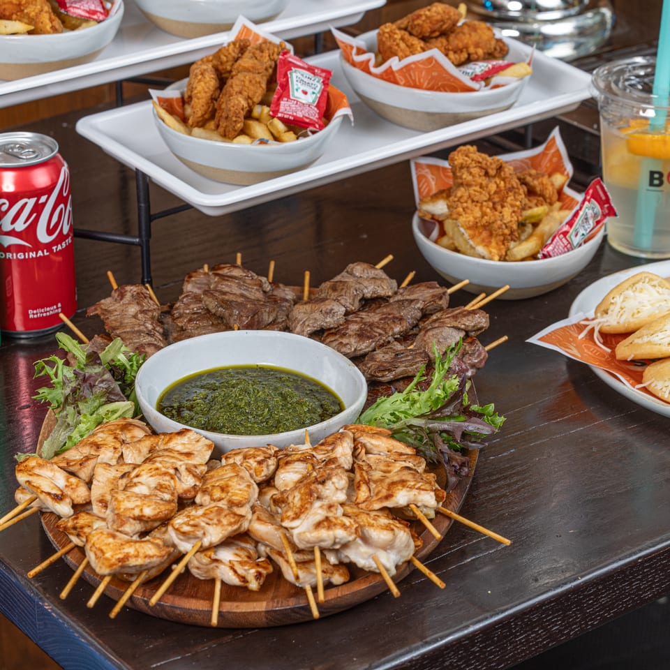 Bocas Grill's Latin-American feast with chicken and beef skewers, green sauce, fries, and drinks.