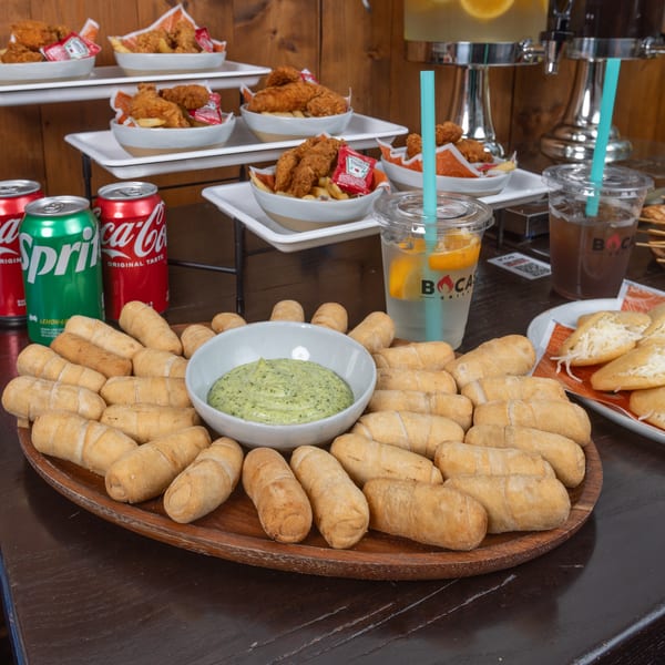 Bocas Grill's Latin-American spread with tequeños, fried chicken, arepas, sodas, and drinks with straws.