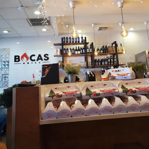 Bocas Grill interior with a counter displaying holiday-themed takeout boxes and shelves of wine bottles.