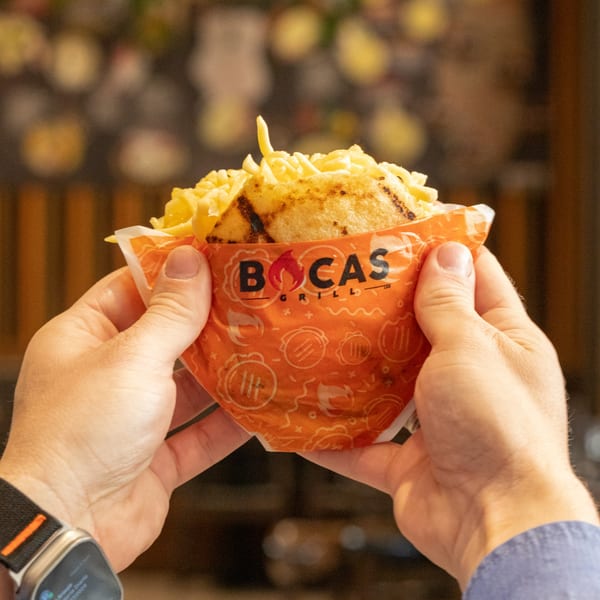 Hands holding a Bocas Grill arepa overflowing with shredded cheese and fries.