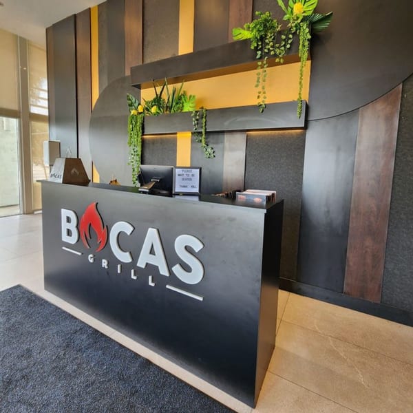 Bocas Grill's dark reception desk with a fiery logo, against a textured wall with plants.