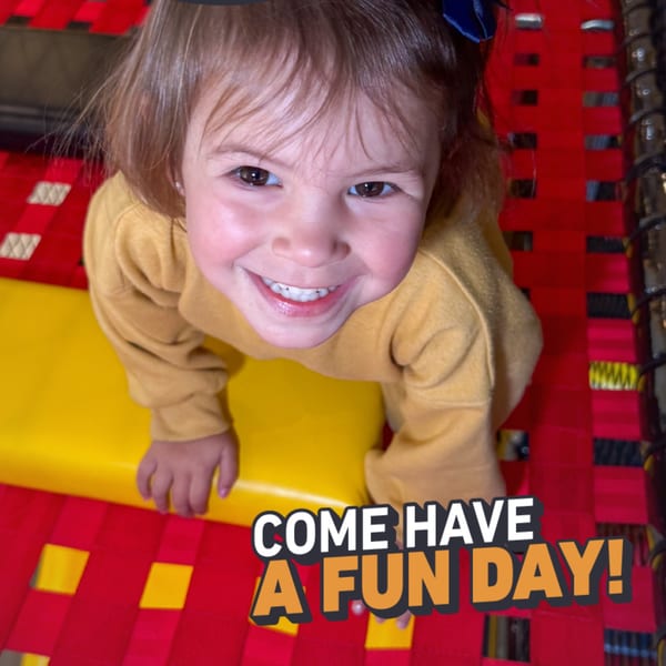 A smiling child in a yellow shirt looks up from a red and yellow play area.