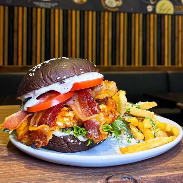 A Bocas Grill burger with bacon, tomato, and sauce on a dark bun, served with fries.