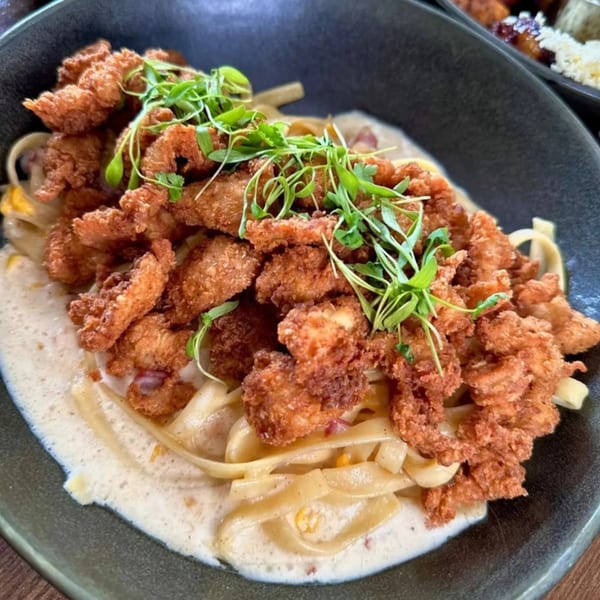 Bocas Grill's fried chicken pieces on a bed of creamy fettuccine pasta, garnished with fresh microgreens.