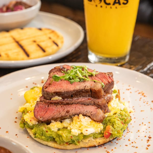 Bocas Grill's steak, scrambled eggs, and guacamole on an arepa, with a drink and another arepa.