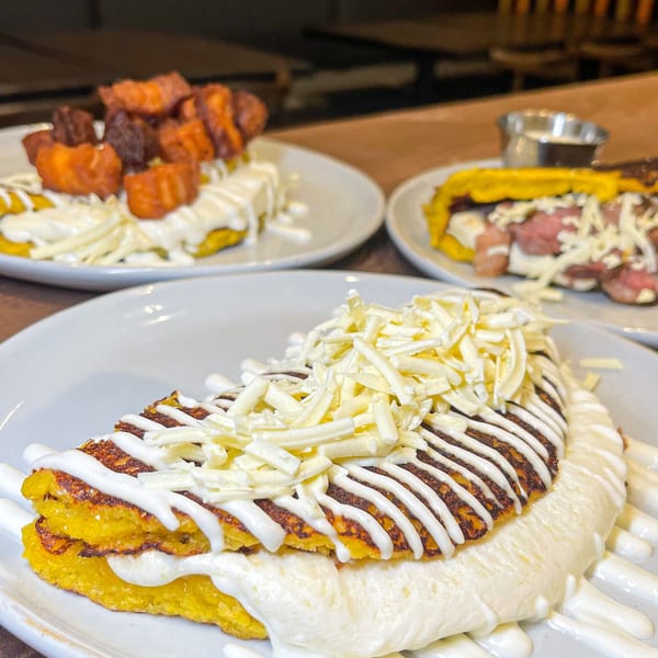 Close-up of a cheesy Latin-American cachapa with cream and shredded cheese, with other dishes blurred in the background.