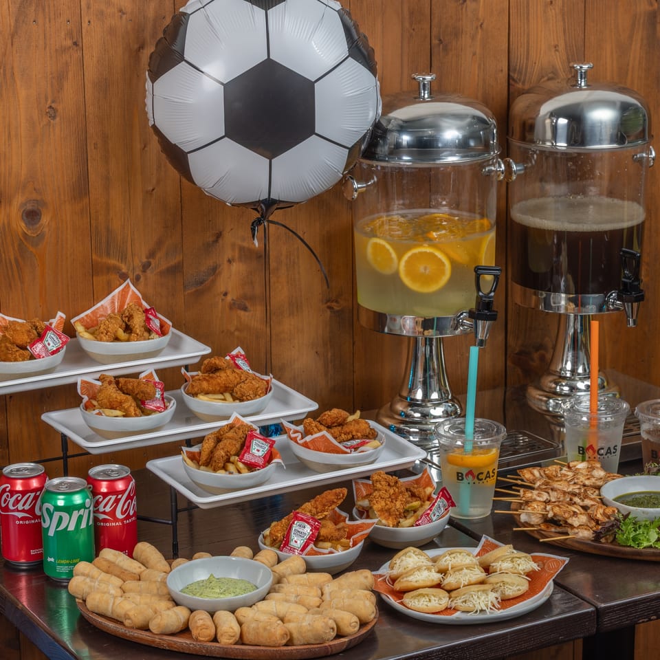 A soccer-themed party spread with Bocas Grill chicken tenders, tequeños, arepas, chicken skewers, and drinks.