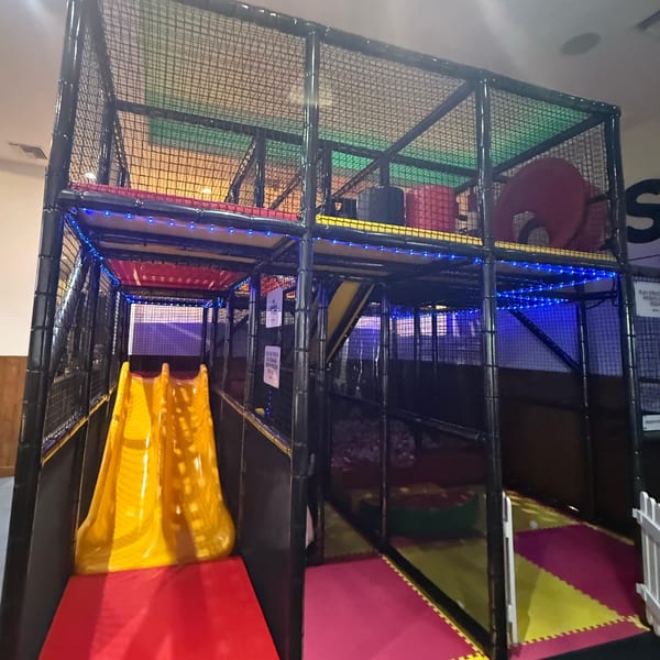 A multi-level indoor playground with a yellow slide, blue lights, and colorful padded flooring.