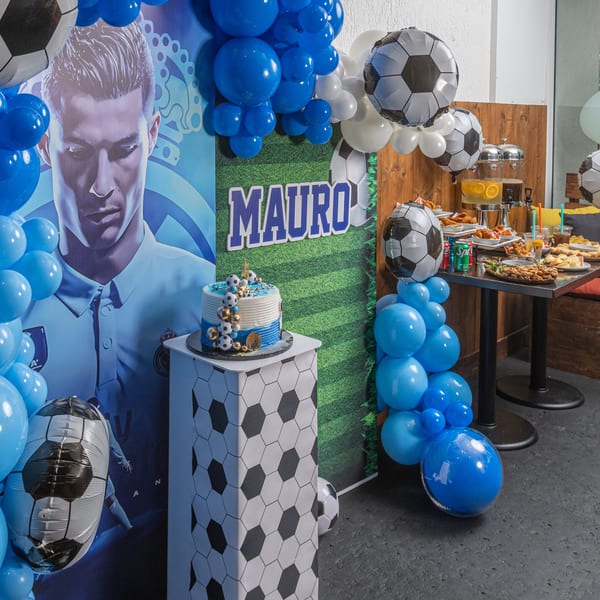 Soccer-themed birthday party with blue balloons, a cake, and a buffet table with drinks and food.
