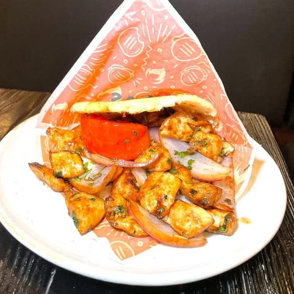 Bocas Grill's Latin-American dish with seasoned chicken, red onions, and a large tomato slice in a pita.