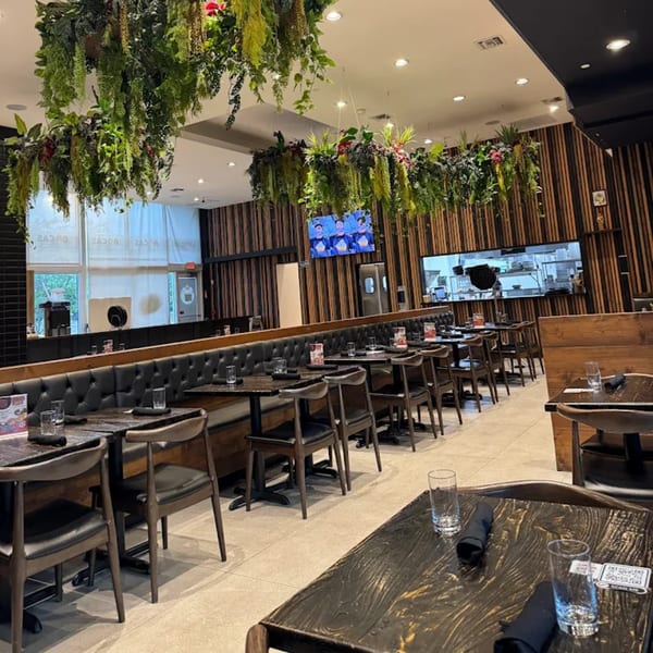 Interior of Bocas Grill, featuring dark wooden tables, black booth seating, and hanging green plants.