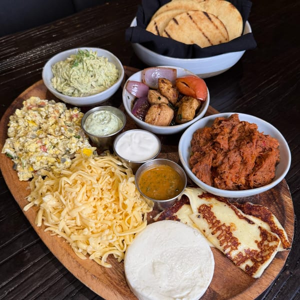A wooden platter with various Latin-American dishes, including shredded chicken, cheeses, and sauces.