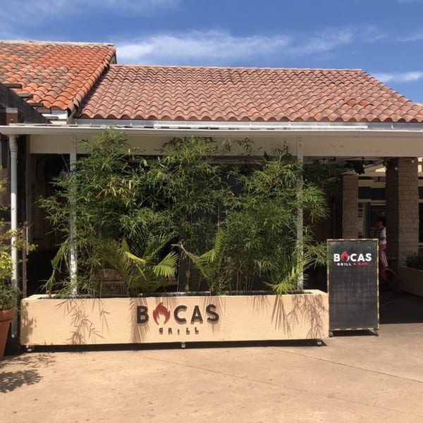 Bocas Grill restaurant exterior with a terracotta roof, lush green plants, and a chalkboard sign.